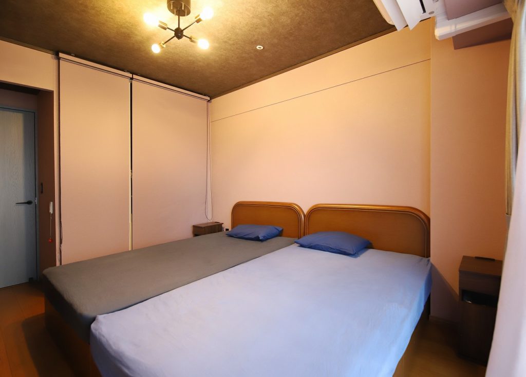 赤土色の壁紙とグレーの天井で落ち着きのある寝室に。収納部のロールスクリーンも同色で壁と一体化>